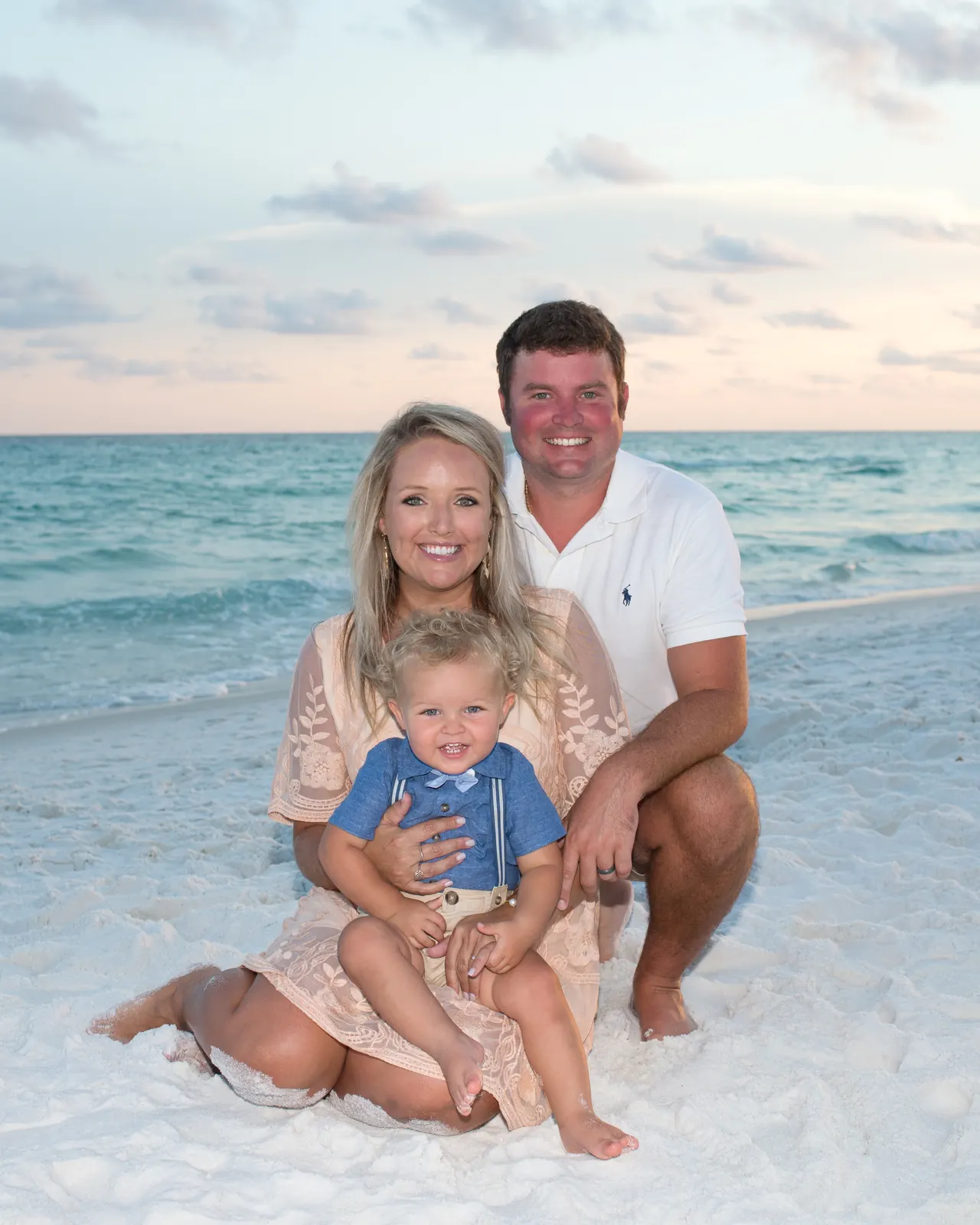 Mom, dad and toddler sitting together in the white sand
