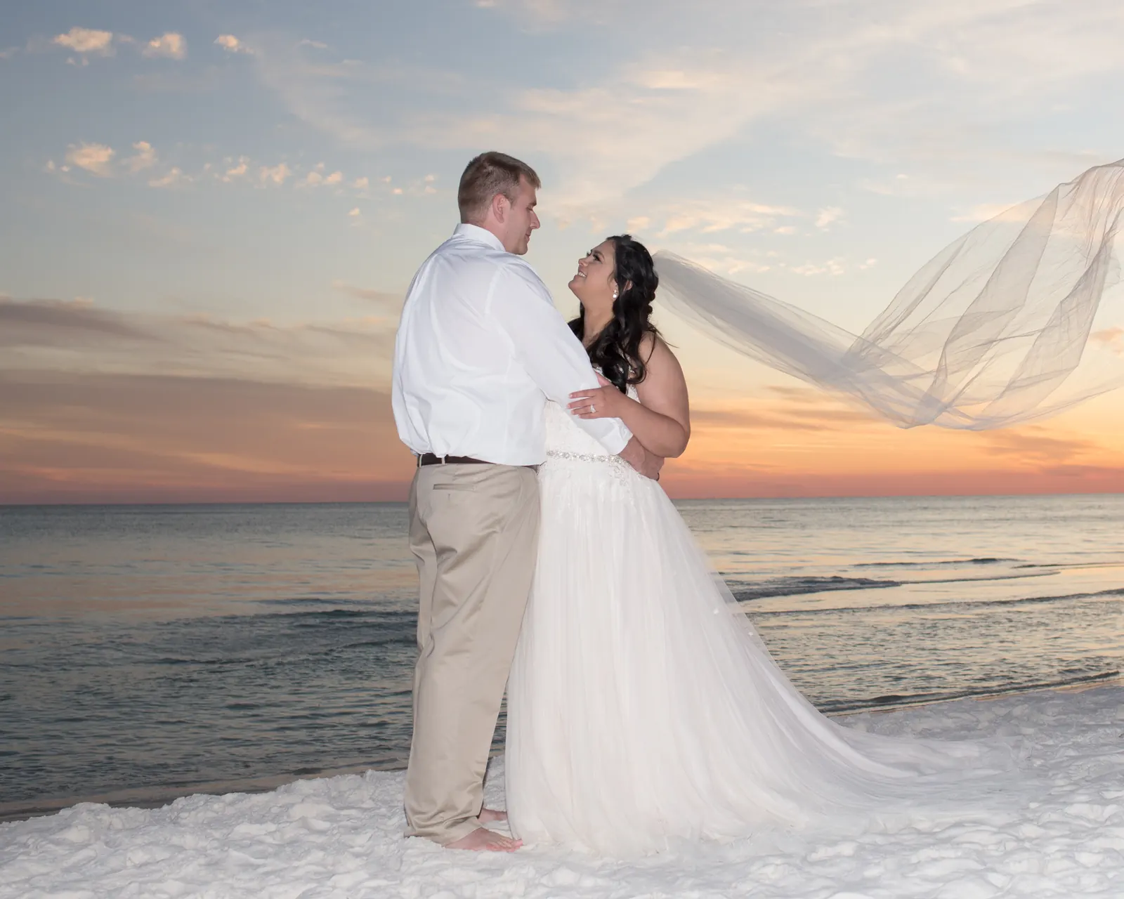 Bride and groom with veil blowing at sunset